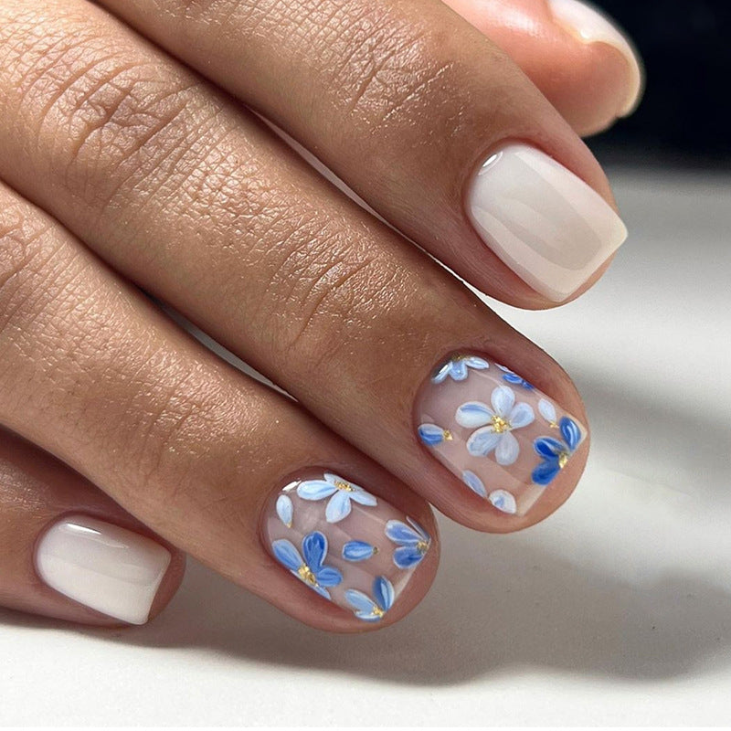 A set of press-on nails featuring blue floral design with gold accents on a white background.