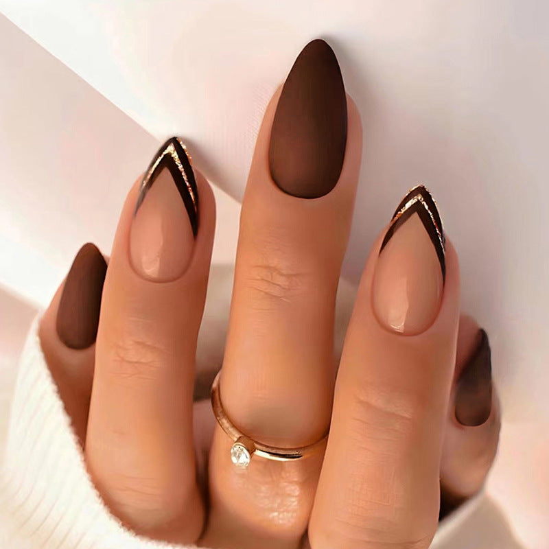 Nail art with dark brown polish and gold tips on a light background