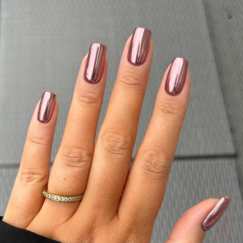 A hand with medium-length coffin-shaped nails painted in a rose gold mirror finish press on nail set.