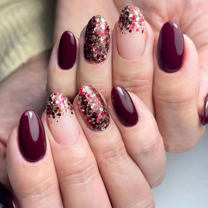 Nails with burgundy polish and glittery accents on a neutral background