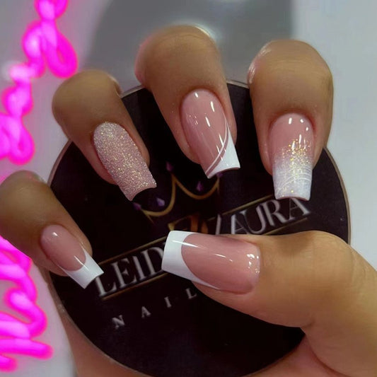 A hand showcasing press-on nails with a medium square shape. The nails are primarily a nude color with a gold glitter design on the tips.