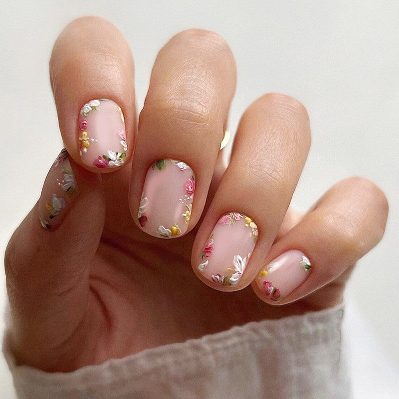 A hand showcasing press on nails with a beige base and floral patterns.