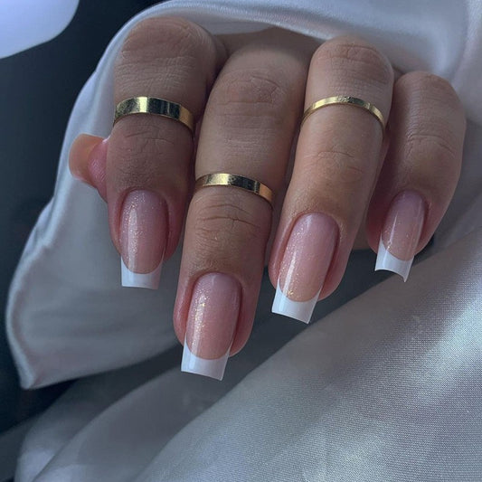 Close-up of a hand with gold rings and French manicure nails on a white background