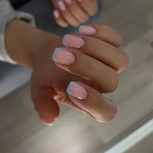 A close-up image of a person's hand with short square-shaped nails featuring a blue French tip and pink embellishments.