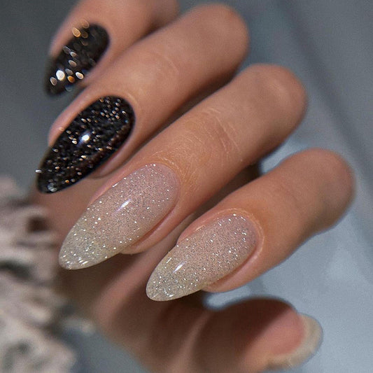 A close-up image of a hand showcasing medium-length oval-shaped nails with a glitter design, transitioning from black to a sparkling finish.