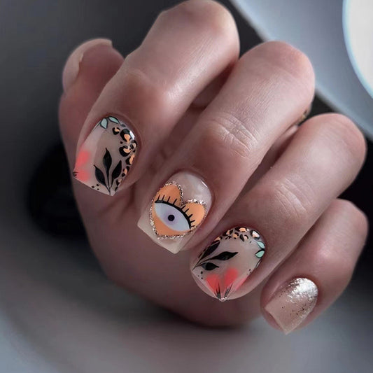 A hand showcasing press-on nails with a multicolor cartoon design, including eyes and floral patterns on a square nail shape.