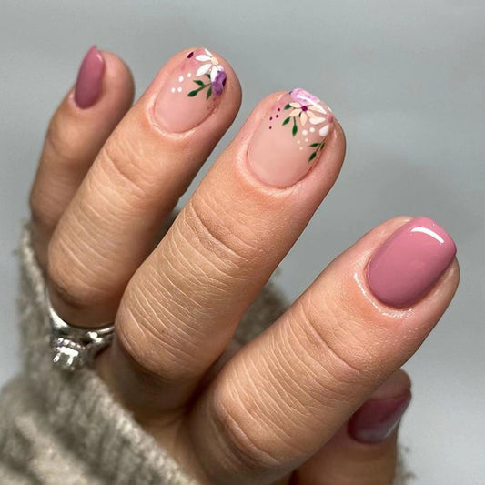 Hand with pink nail polish and floral designs on a neutral background