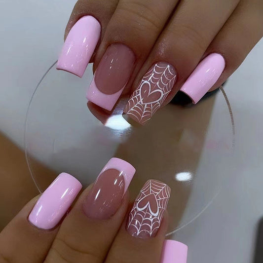 A hand showcasing press-on nails with a medium square shape in pink shades, some with a heart pattern.