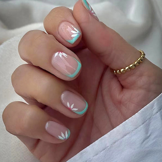 A hand with beige press-on nails featuring a floral pattern with pink and blue accents.