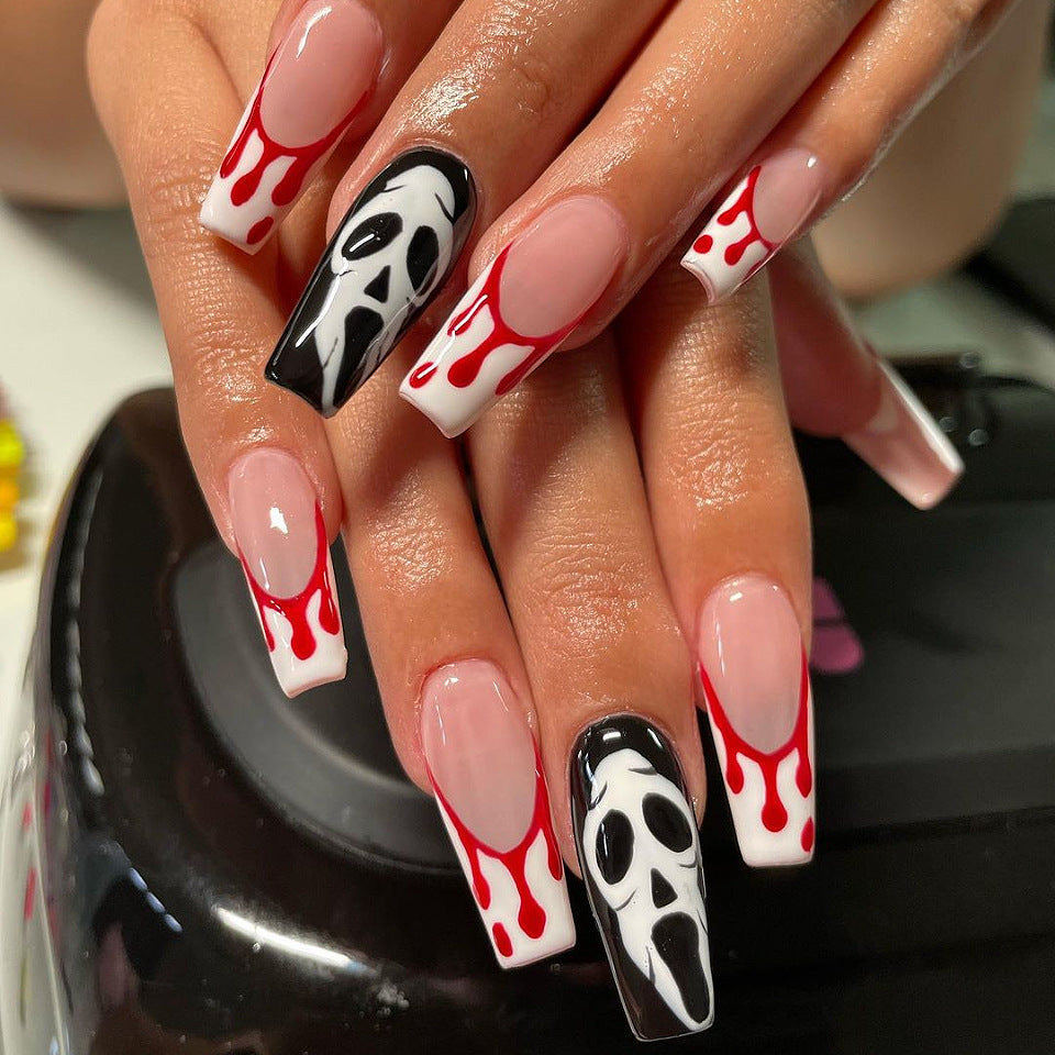 A set of long coffin-shaped press-on nails with a white base and Halloween motif, including the phrase 'SCREAM AT US' and images of bones and blood droplets.