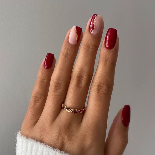 Hand with red nail polish and a gold ring on a gray background