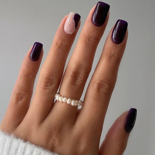 A set of short square deep plum press on nails with rhinestone accent on one nail, displayed on a hand wearing a white sweater.