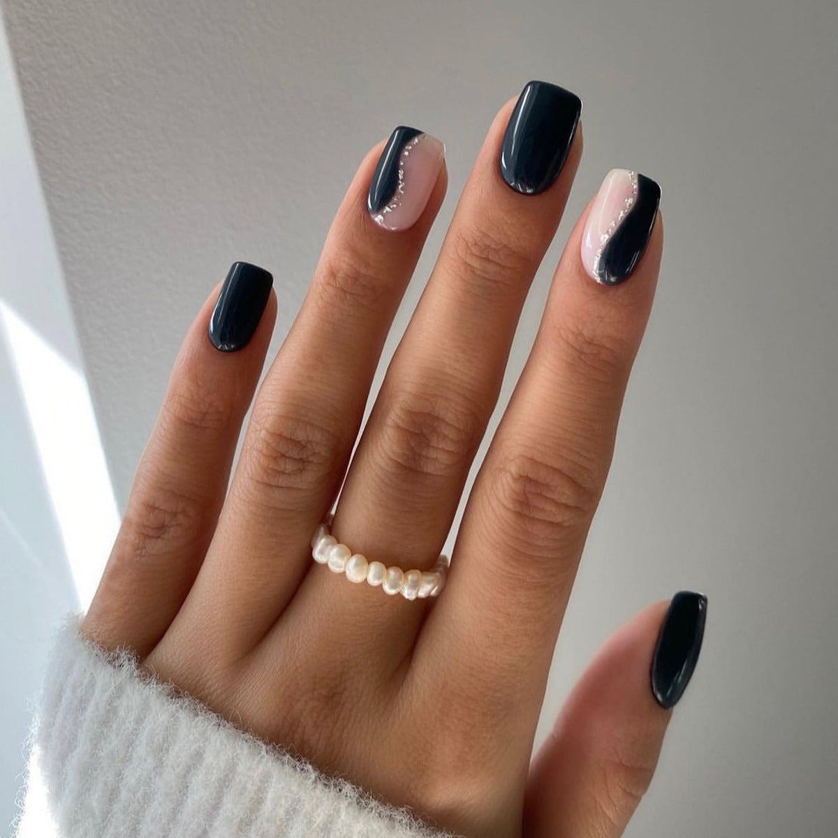 Hand with dark nail polish and a pearl ring on a neutral background