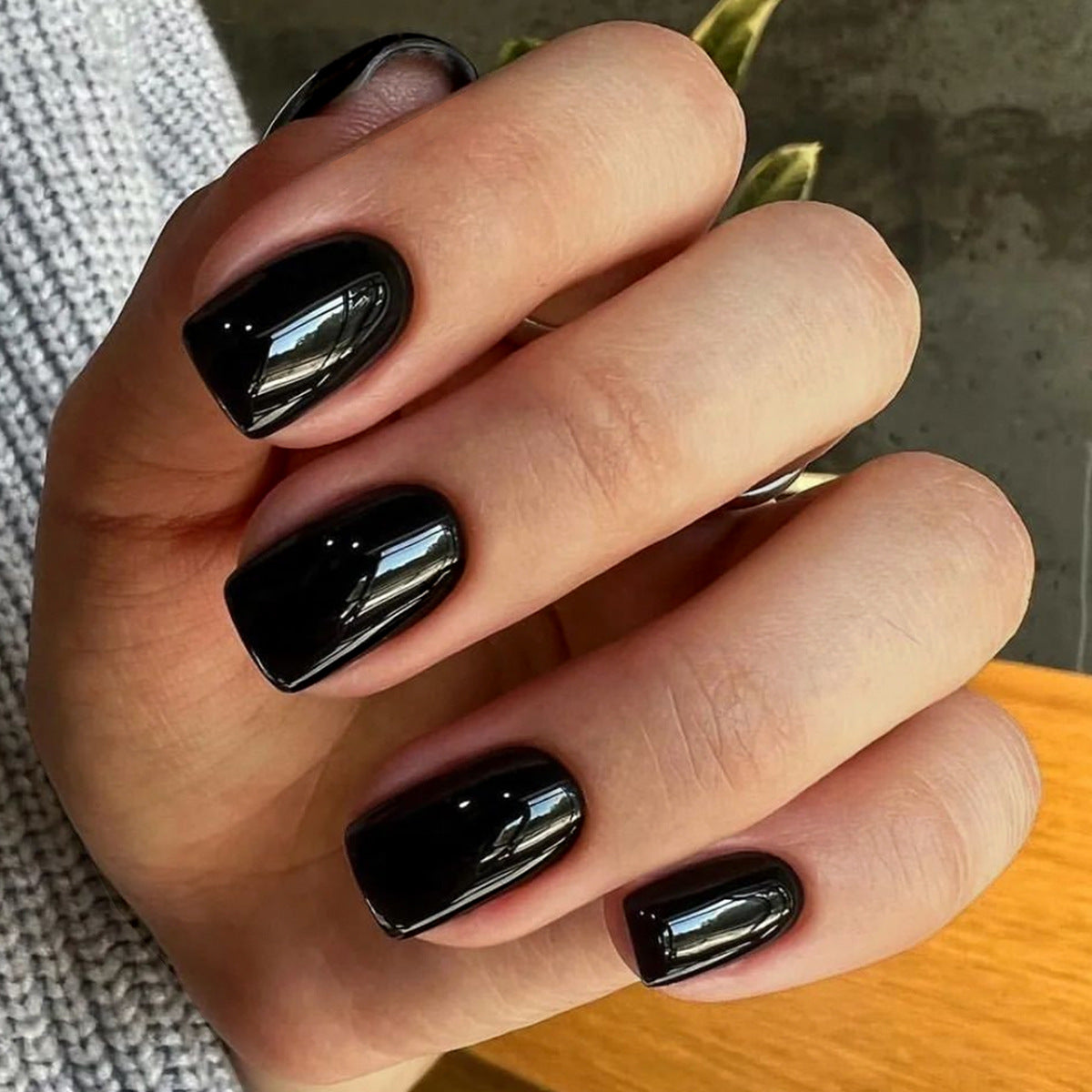A hand with glossy black press-on nails in a short square shape.
