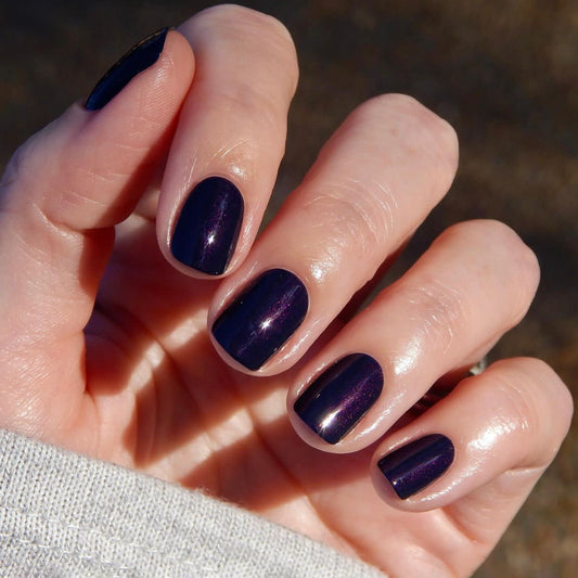 Hand with dark purple nail polish on a blurred natural background