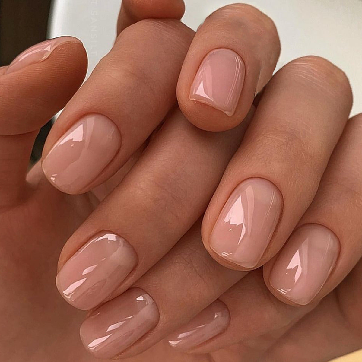 A pair of beige press-on nails with a high shine finish, displayed on a hand.