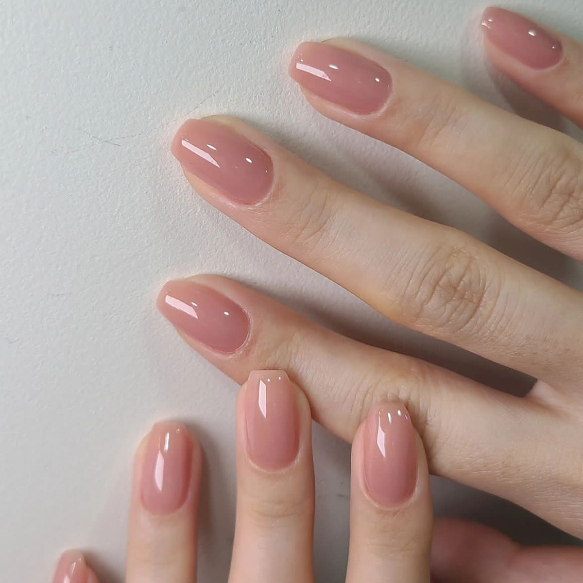 Close-up of a hand with pink nail polish on a light gray background