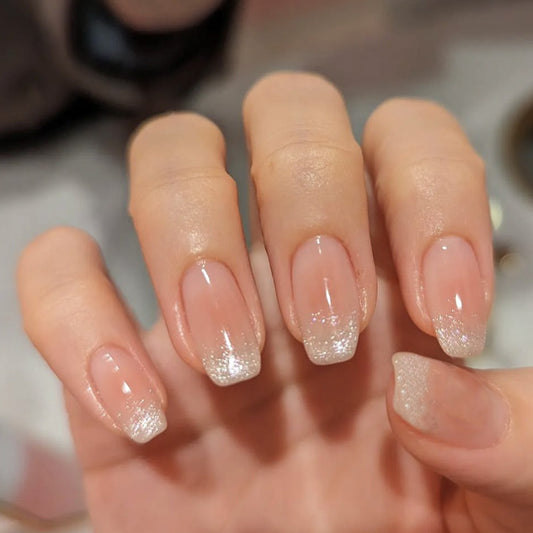 A hand with beige press-on nails with glitter and a square shape, featuring a fingernail design.