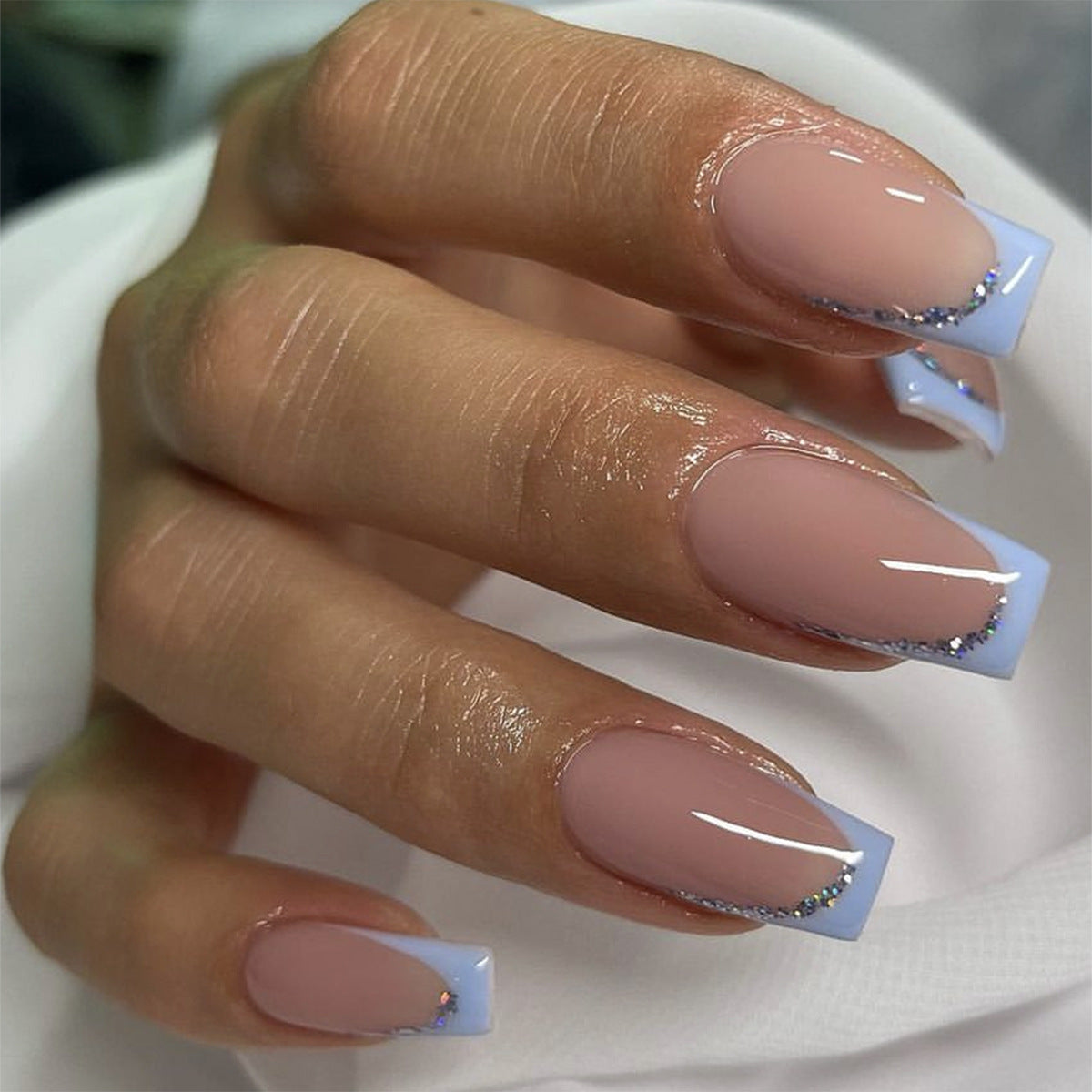 A pair of medium coffin beige press-on nails with baby blue tips and silver glitter detail.
