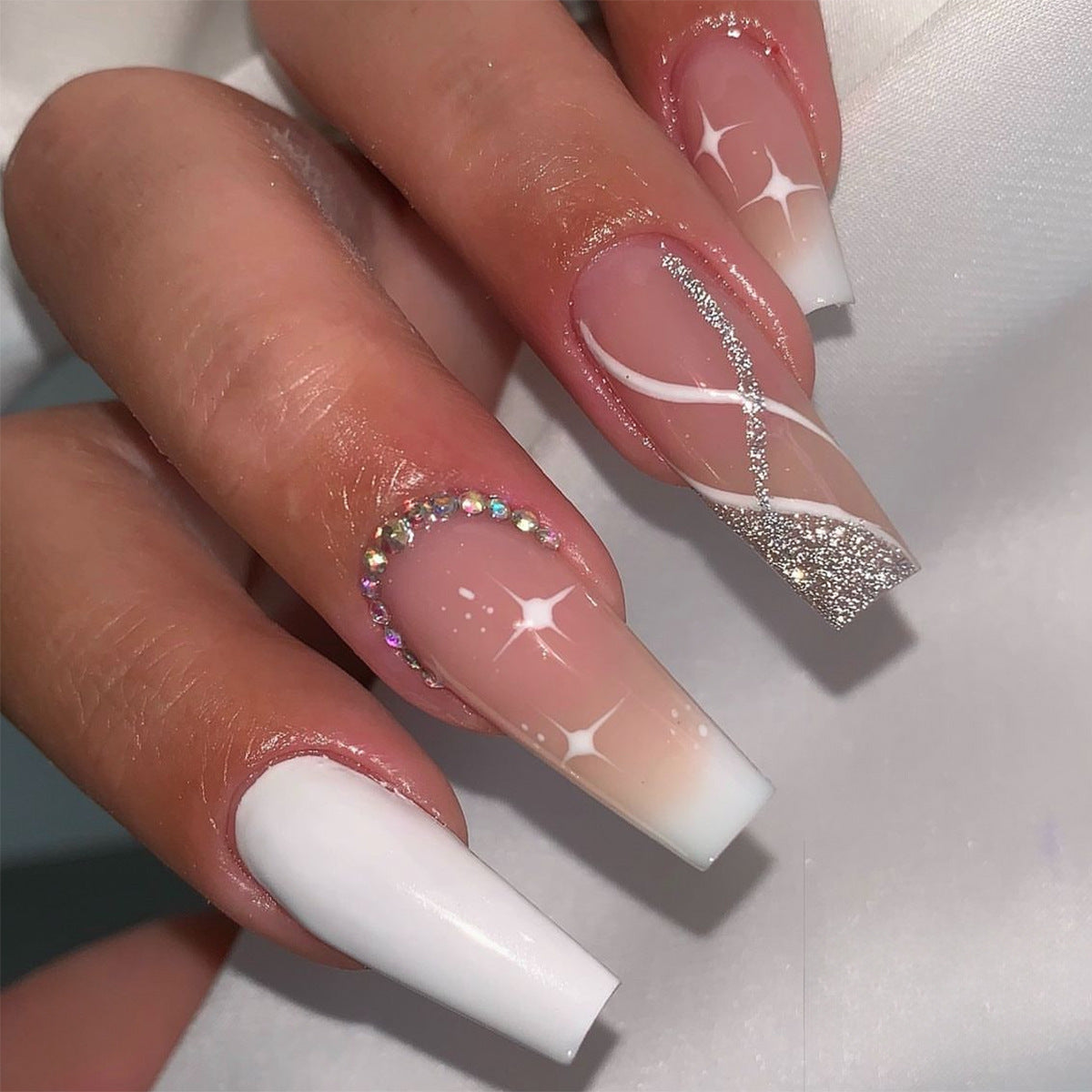 Close-up of a hand with decorative nails featuring white, pink, and silver designs on a light background.
