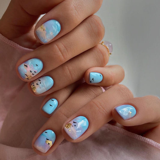 Hand with blue and pink nail art featuring cloud and cloud face designs.