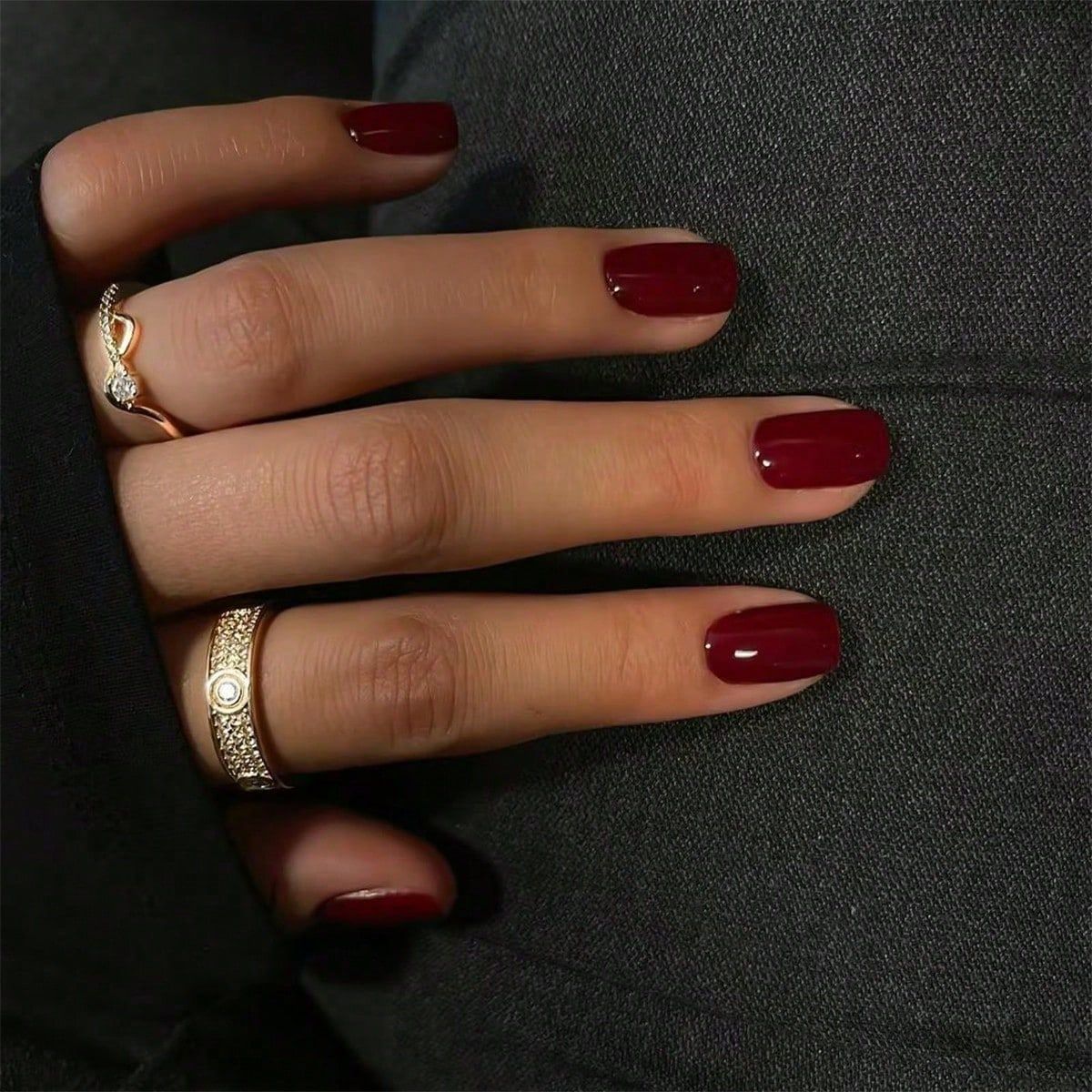 A person showing off their deep burgundy colored nails with a glossy finish, alongside a ring on their finger.