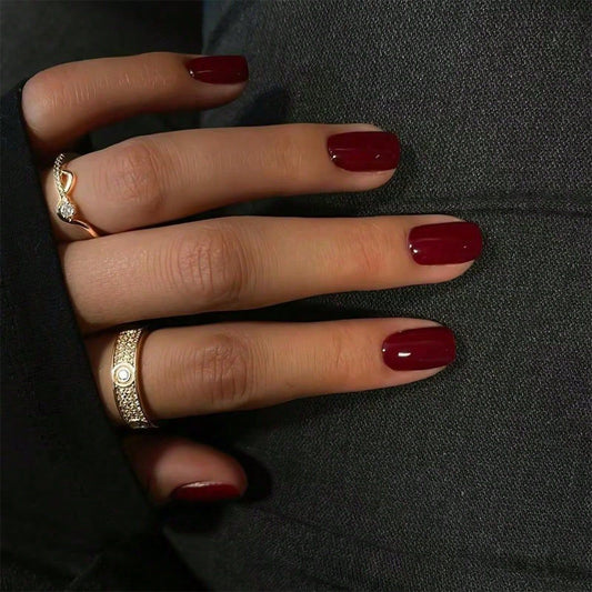 A person showing off their deep burgundy colored nails with a glossy finish, alongside a ring on their finger.