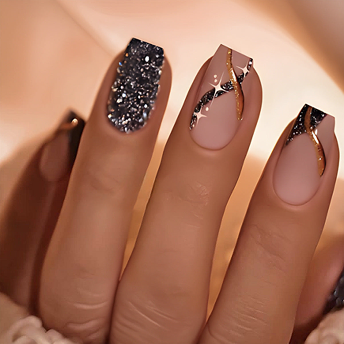 A set of press-on nails featuring a medium coffin shape in black and beige with gold swirls and glitter accents.