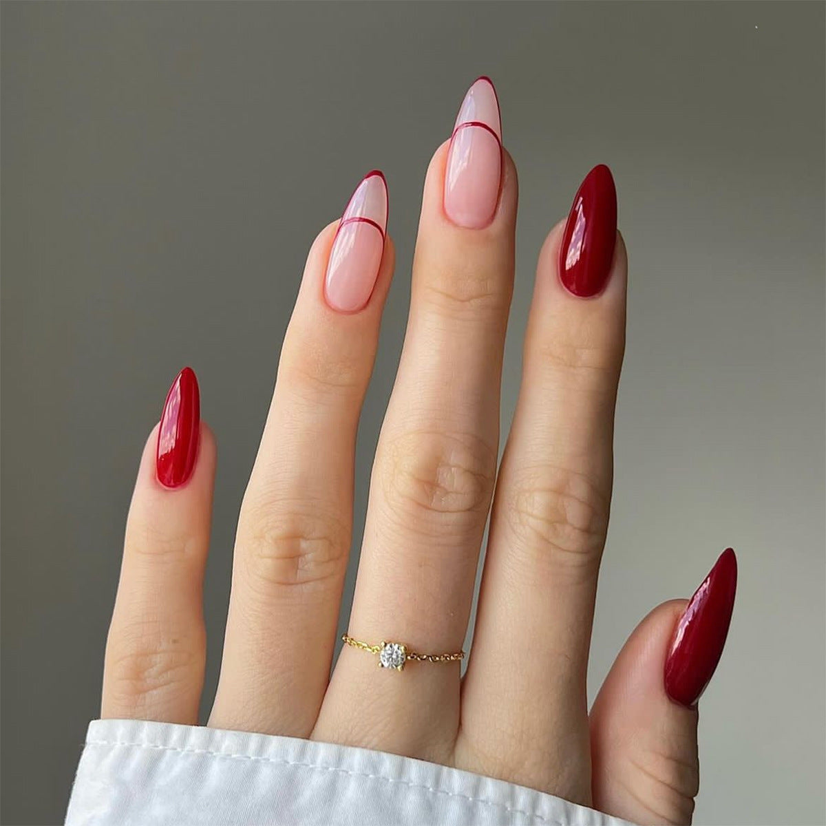 A set of long, almond-shaped, beige to red ombre press-on nails with a line art design.