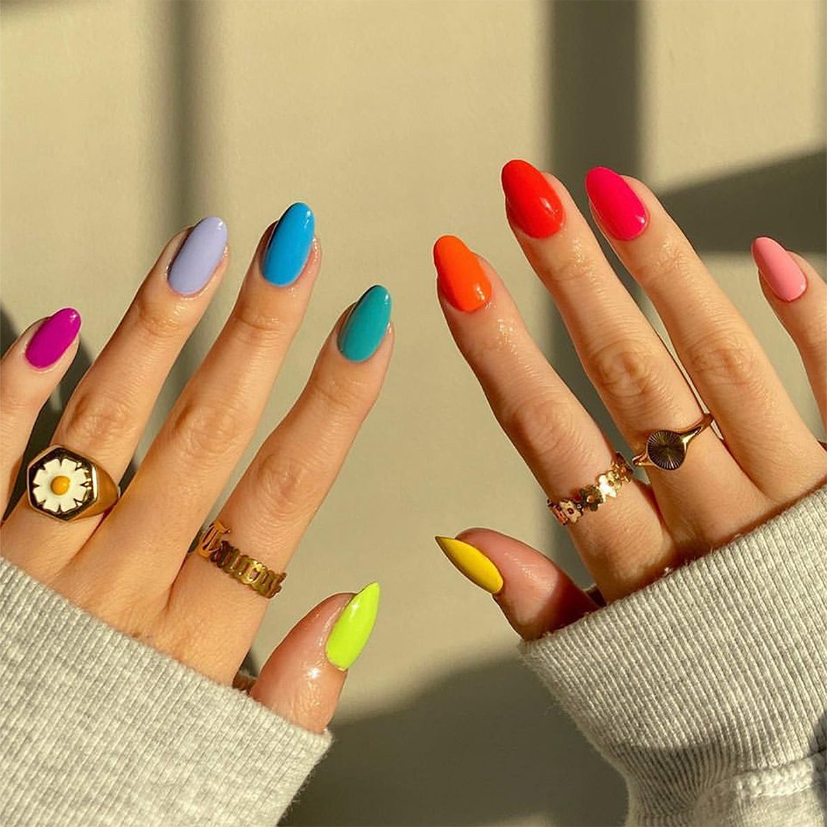 A set of press-on nails in assorted bright colors, including pink, blue, green, yellow, and red, applied to almond-shaped nails.