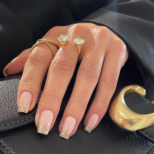 Hand with gold rings and glittery nails on a black leather surface