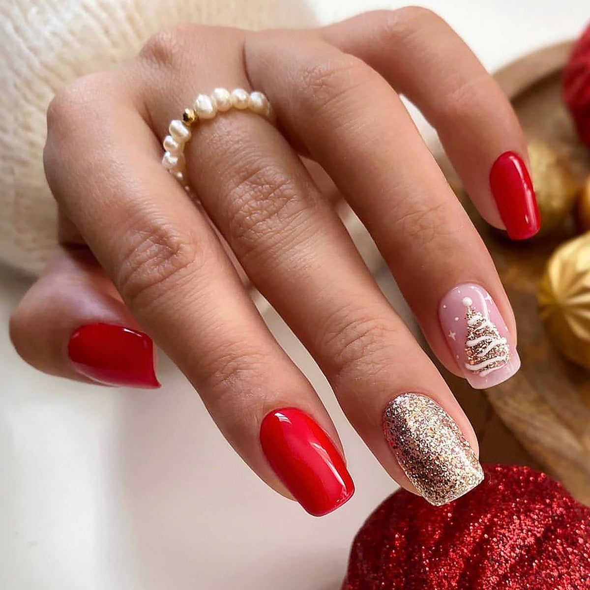 Close-up of a hand with red and gold nail polish, wearing a pearl ring.