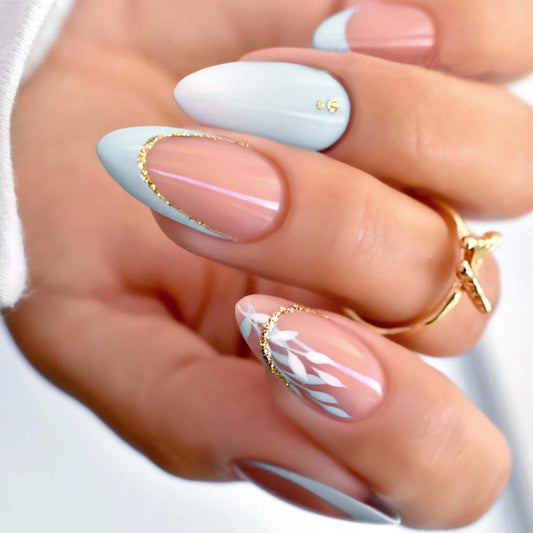 A hand showcasing press-on nails with a medium almond shape. The nails are primarily blue with white tips and gold detailing.