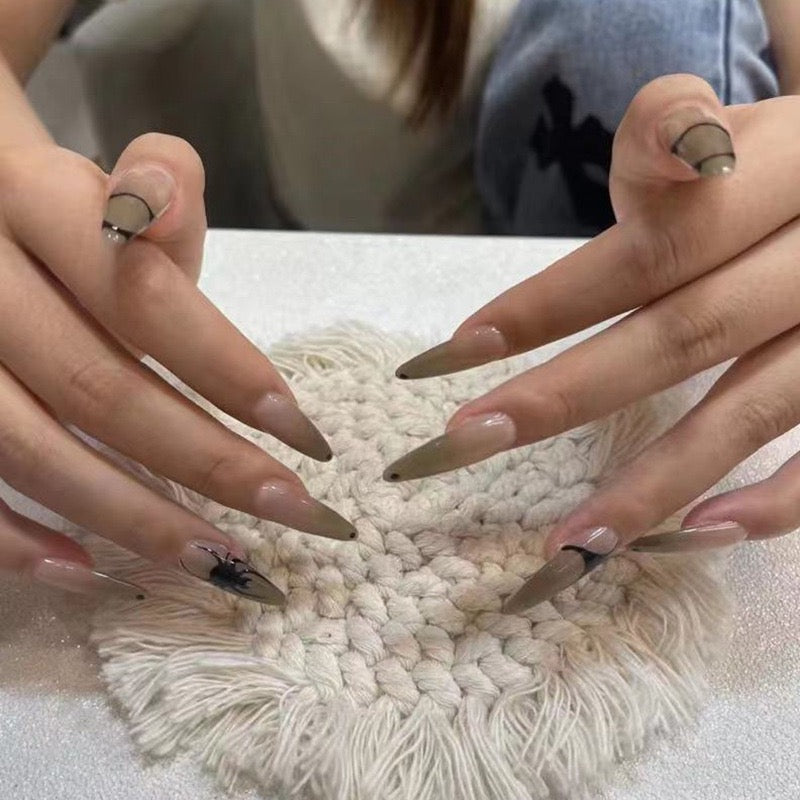 A person's hands showcasing long beige stiletto nails with a spider web design, placed on a white textured surface.