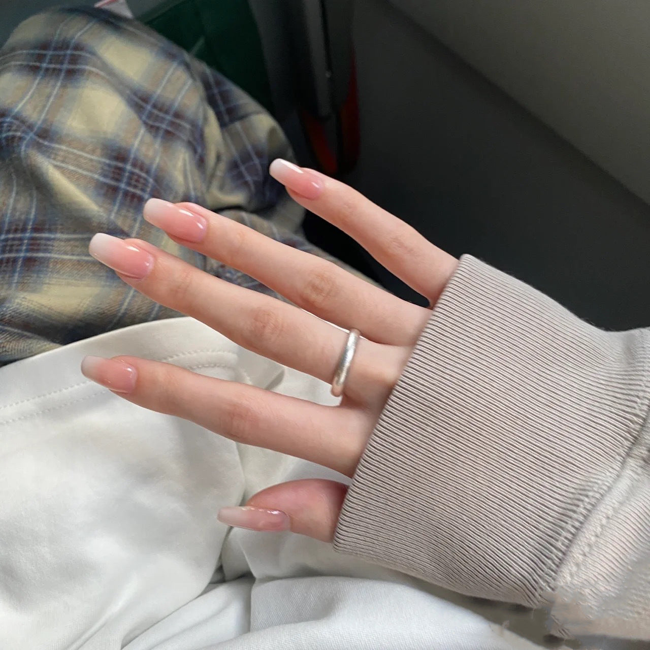 Close-up of a hand with a ring, wearing a beige sleeve, with plaid pants and white shirt in the background.