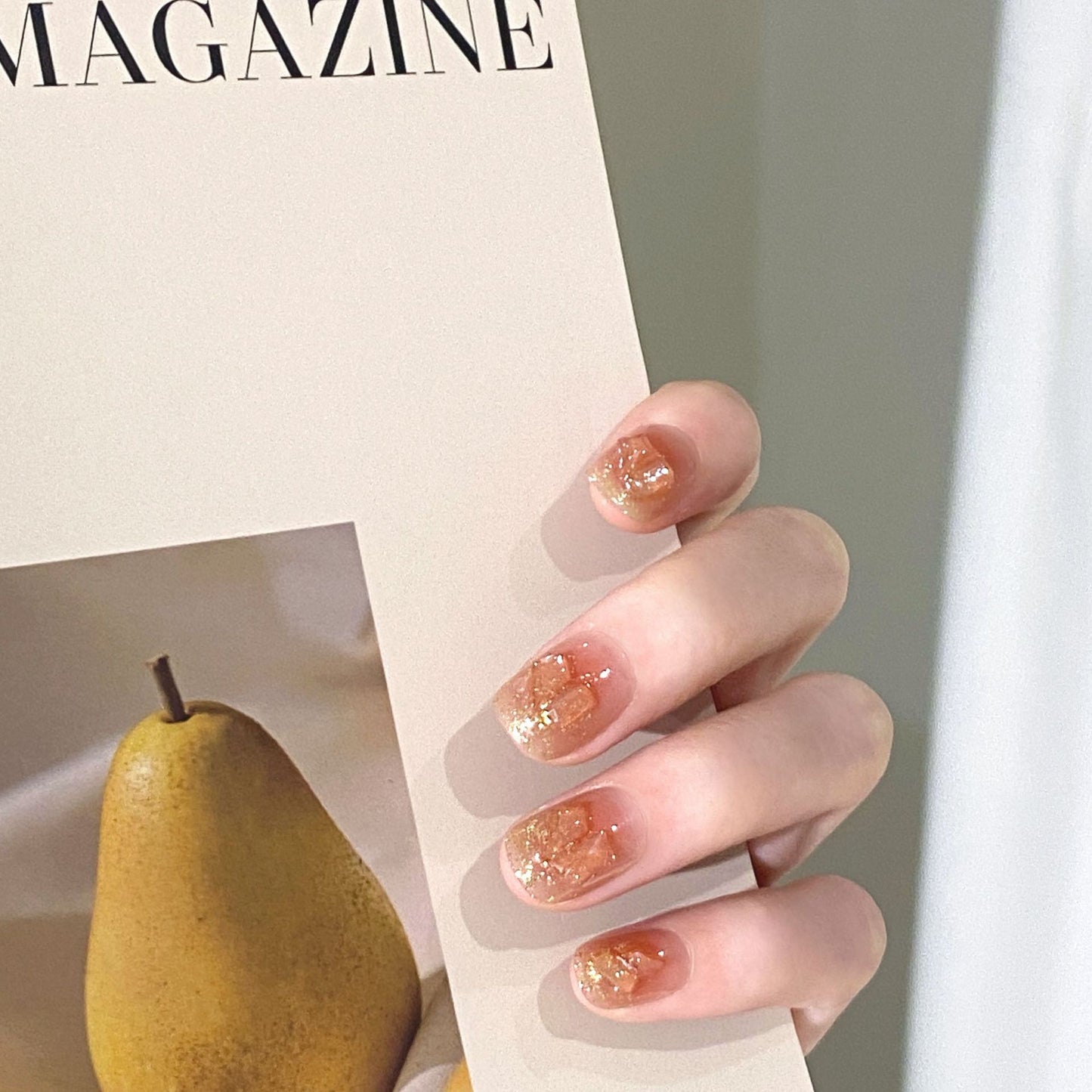 Close-up of a hand with glittery nail polish holding a magazine featuring a pear.