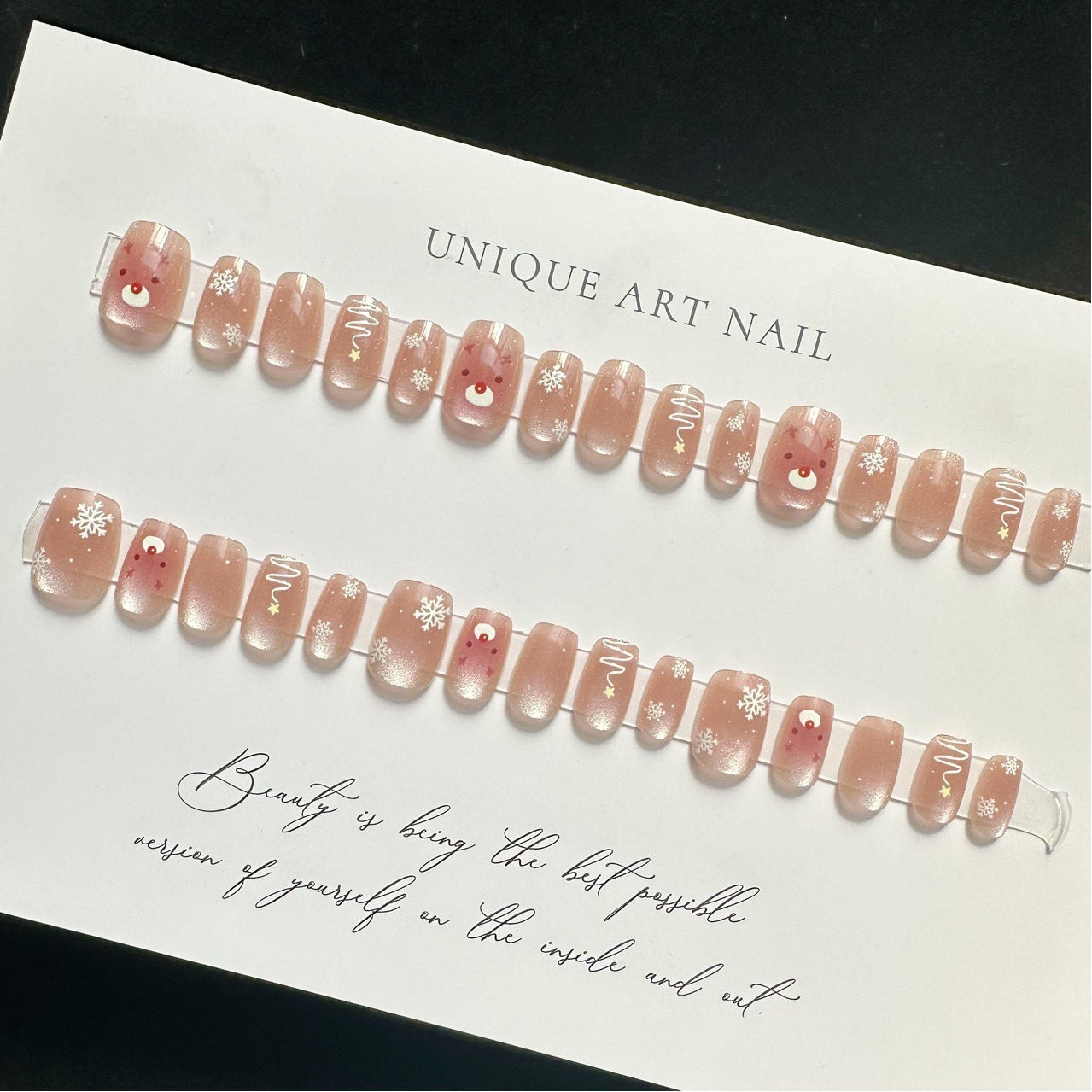 A set of pink press-on nails with snowflake accents and a reindeer design, displayed on a white background.