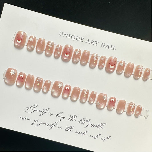 A set of pink press-on nails with snowflake accents and a reindeer design, displayed on a white background.