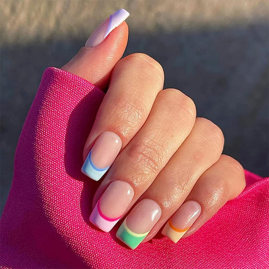 A hand with medium square press-on nails featuring a rainbow French tip design with ombre effect in pastel colors.
