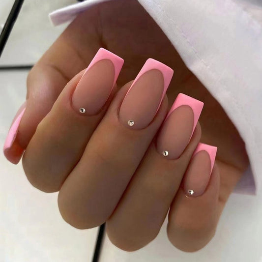 A hand with medium square pink French tips press on nails with rhinestone embellishments.