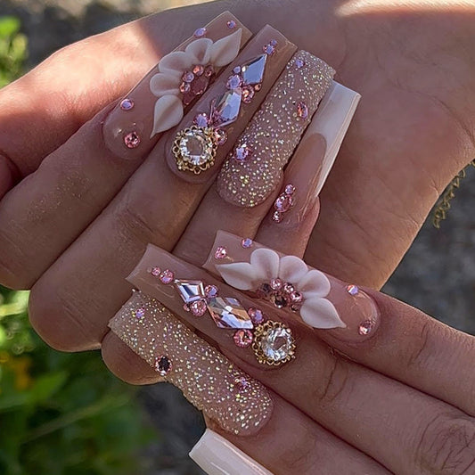 Decorative false nails with flowers and rhinestones held in a hand.
