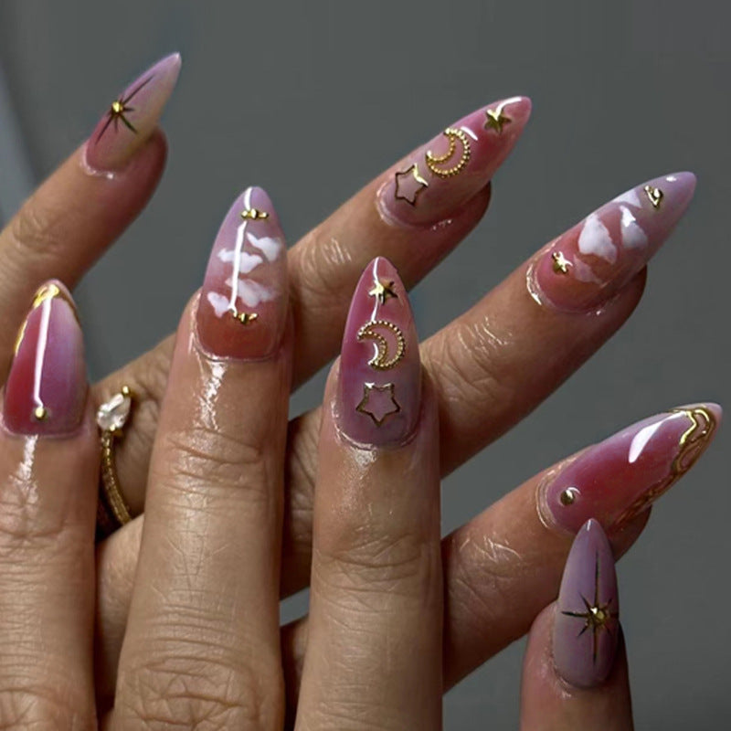 A hand showcasing medium almond pink press-on nails with gold star and moon patterns.