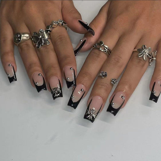 A set of press-on nails featuring a medium square shape with a black tip and clear tip design, embellished with small silver embellishments.