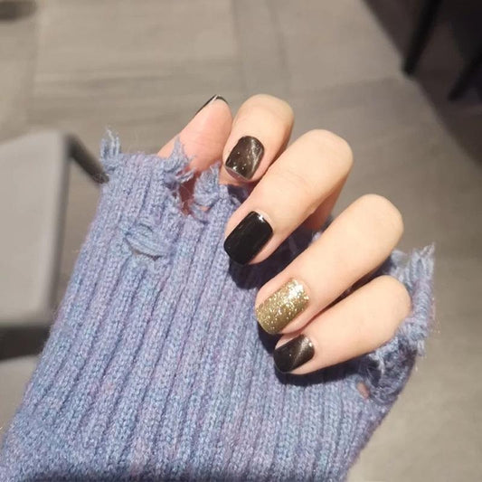 A hand with false nails painted in black and glittery gold colors, holding a blue textured object.